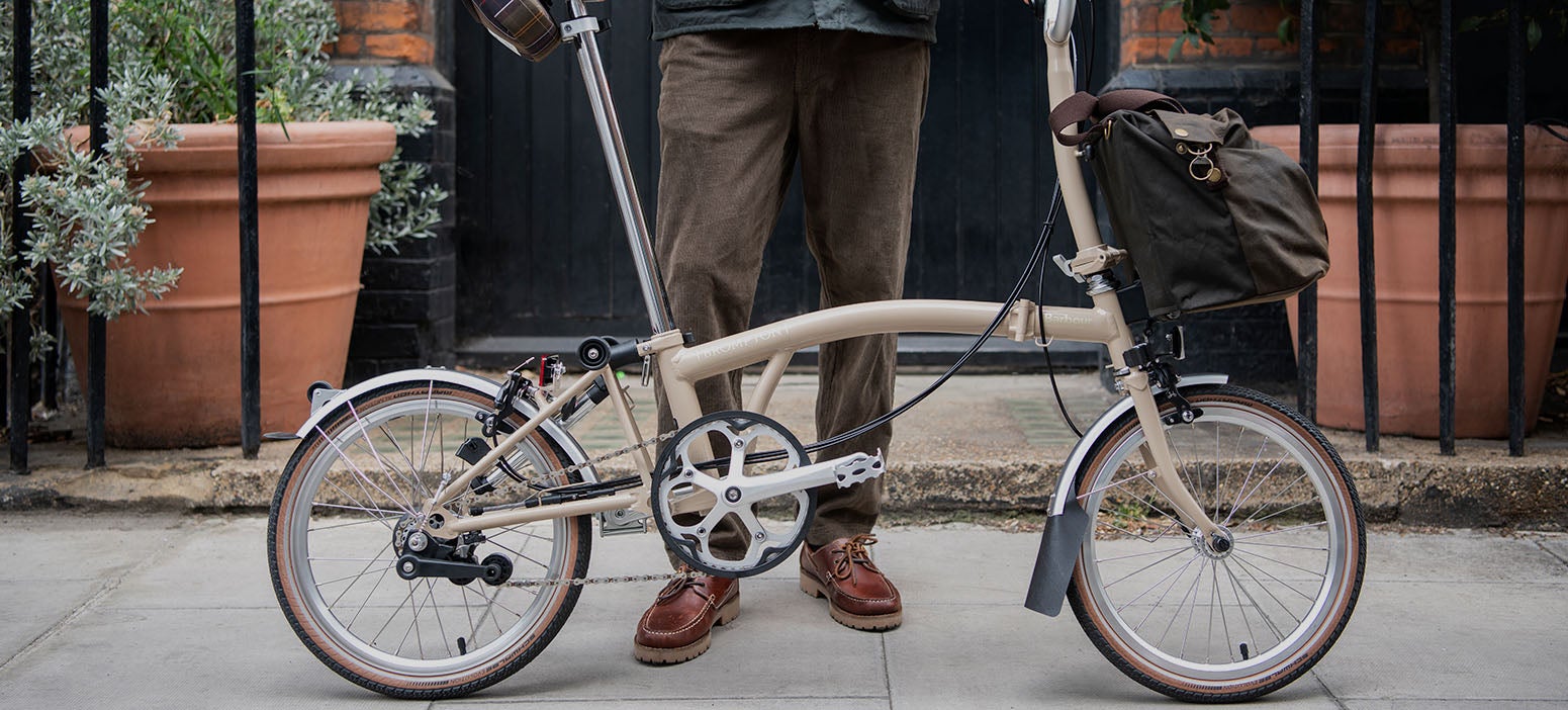 Une femme conduisant un Barbour x Brompton Special Edition C Line Explore avec un sac fourre-tout devant et portant la veste Bromdale pour femme.