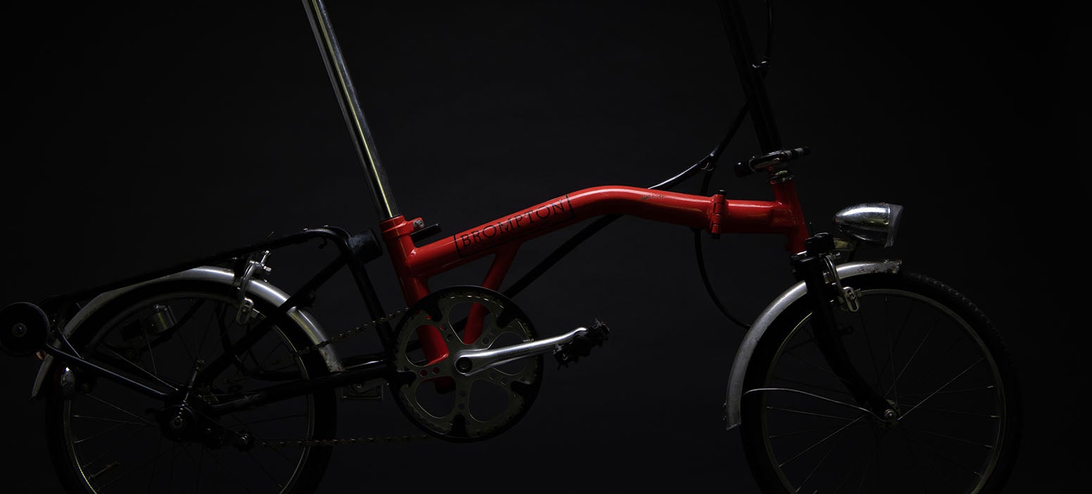 Un Brompton MK 1 rouge sous les projecteurs