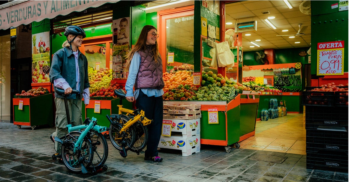 Deux personnes avec des lignes C pliées marchant devant un marchand de fruits et légumes