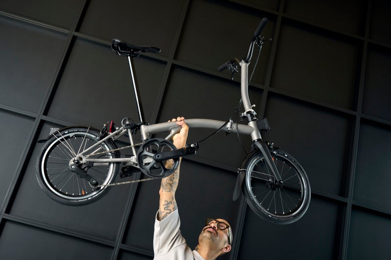 personne tenant un vélo de la marque Brompton au-dessus de sa tête