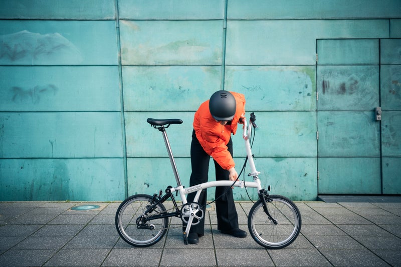 person in orange jacket folding a Brompton A Line bike