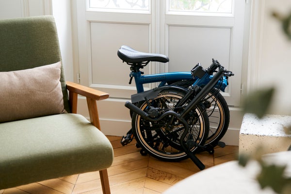 Un vélo pliant Brompton rangé à côté d'un fauteuil du milieu du siècle