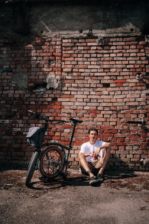 man sat in front of brick wall with brompton g line bike