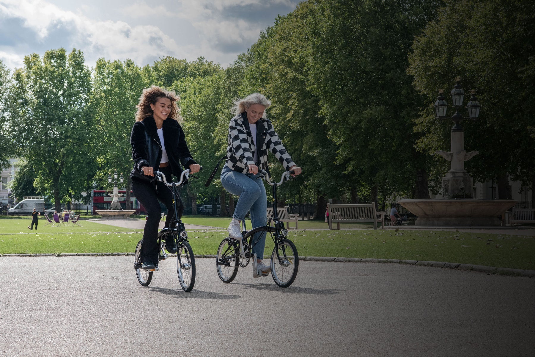 Two people riding Brompton bikes through park