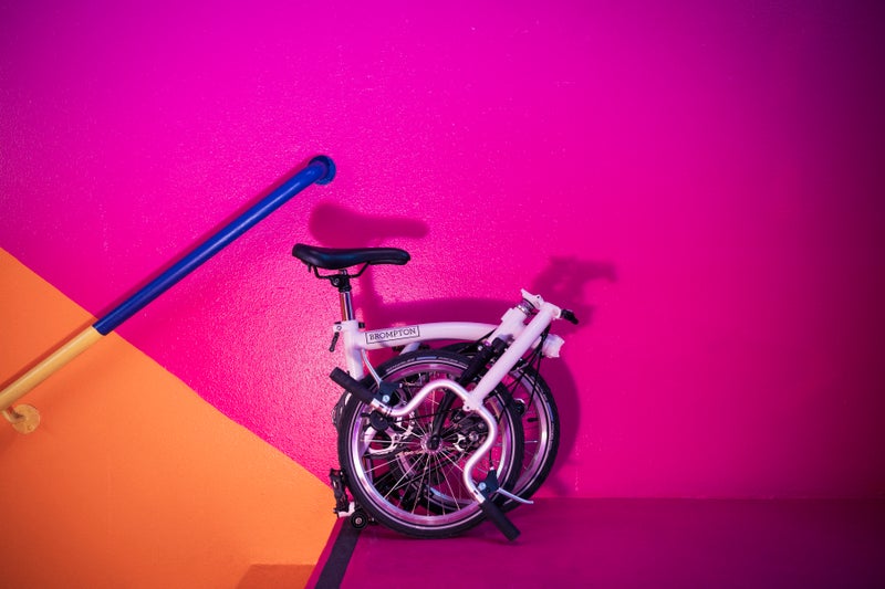 folded A Line brompton bike in front of pink and orange wall