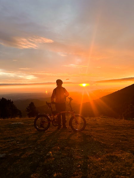 Silhouette of a person with a Brompton bike on a mountain at sunset