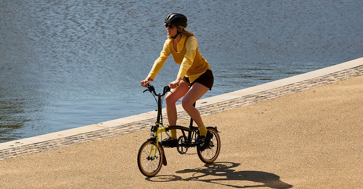 Woman riding Brompton x Tour de France C Line by the river