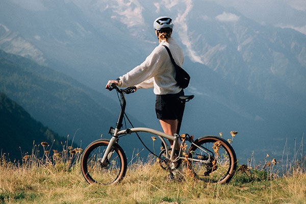 Une personne se tient au sommet d'une montagne avec un vélo Brompton G Line.