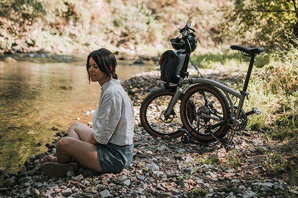 Une personne assise avec un vélo G Line plié sur la rive d'une rivière