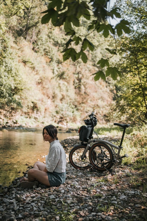 woman sat by river with a brompton g line bike