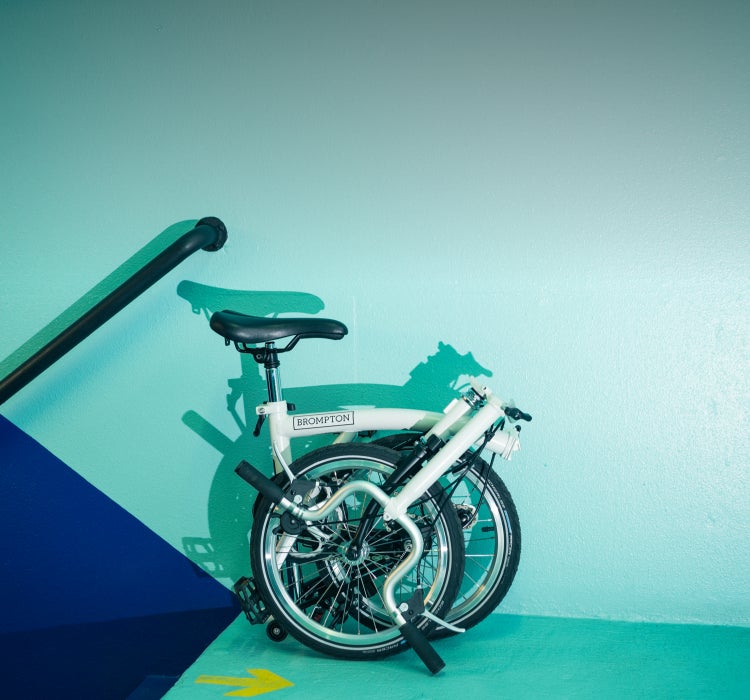 Un Brompton A Line plié contre un mur bleu sarcelle et bleu marine