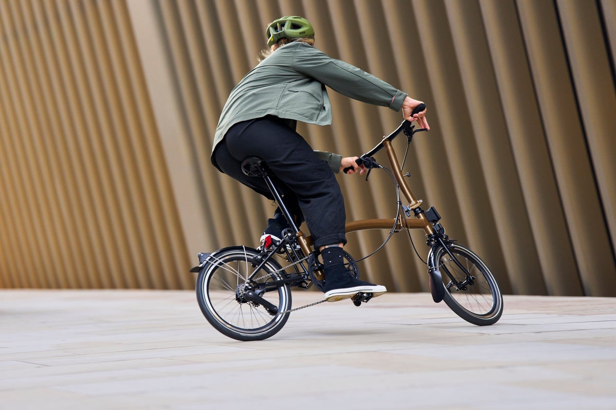 person in green jacket riding the brompton bronze sky in front of a brown background