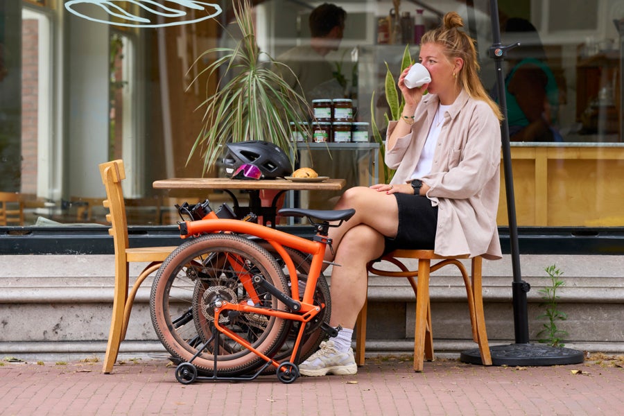 Une personne assise à l'extérieur d'un café avec un vélo Brompton G Line plié.