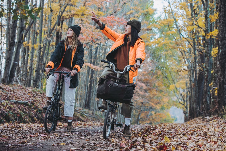 Deux femmes sur des Barbour x Brompton C Line traversant la forêt en vestes Barbour x Brompton
