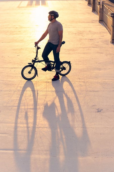 person rolling a folded brompton p line against a yellow backdrop