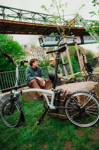 man sitting on a wall with a folded bolt blue brompton p line beside him