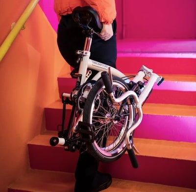 person carrying a folded brompton a line bike upstairs