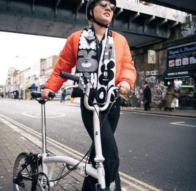 person wheeling a brompton a line bike down a road in london