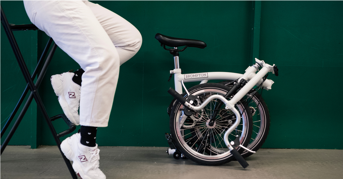 Person sitting on a stool next to a white Brompton against a dark green wall